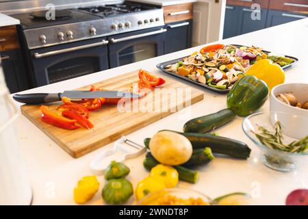 Eine Küchenzeile zeigt verschiedene Gemüse und ein Schneidebrett mit geschnittenen roten Paprika Stockfoto