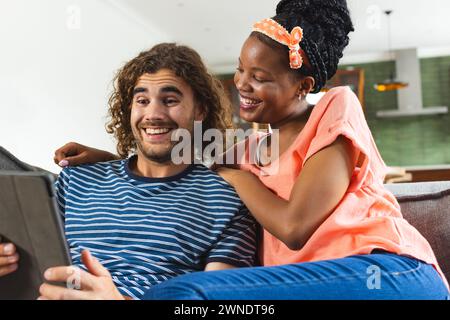 Verschiedene Paare, junge Afroamerikanerin und junger Kaukasier, teilen sich eine Tafel und lächeln zusammen Stockfoto