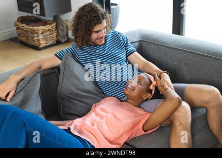 Verschiedene Paare, junger Kaukasier und Afroamerikanerin entspannen sich auf einem grauen Sofa Stockfoto