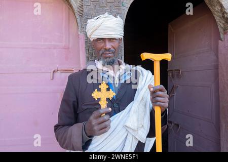 Äthiopischer Mann alter Priester in traditioneller Kleidung, der einen Stock und ein Handkreuz in der Hand vor einer Tür hält. Äthiopien Stockfoto