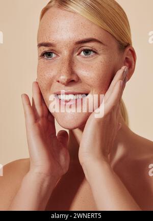 Sehr detailliertes Porträt einer jungen lächelnden Frau, die ihr Gesicht massiert. Nahaufnahme einer blonden Frau, die ihre Haut berührt. Stockfoto