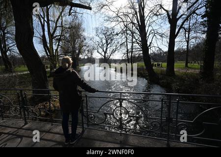 München, Deutschland. März 2024. Ein Wanderer steht auf der Eisbachbrücke im Englischen Garten und genießt die warmen Temperaturen und den Sonnenschein. Quelle: Felix Hörhager/dpa/Alamy Live News Stockfoto