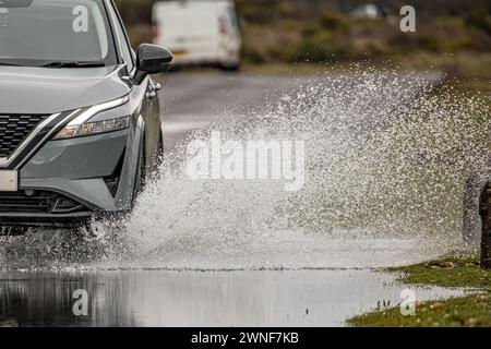 Wasserspritzer aus einem Autorad und dem vorderen Teil des Fahrzeugs, während es durch eine überflutete Straße fährt Stockfoto