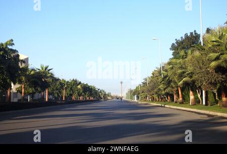 Kairo, Ägypten, 16. Dezember 2023: New Cairo City Street mit Grünflächen auf beiden Seiten von Gehwegen, Gras, Bäumen und Palmen, New Cairo ist ein Satell Stockfoto