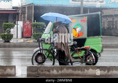 Hyderabad, Pakistan. März 2024. Der Pendler hält einen Regenschirm über dem Kopf, um sich vor Regen zu retten, und bewegt sich während der Regenzeit in Peshawar am Samstag, den 2. März 2024 in Richtung ihres Ziels. Quelle: Pakistan Press International (PPI)/Alamy Live News Stockfoto