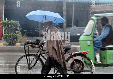 Hyderabad, Pakistan. März 2024. Der Pendler hält einen Regenschirm über dem Kopf, um sich vor Regen zu retten, und bewegt sich während der Regenzeit in Peshawar am Samstag, den 2. März 2024 in Richtung ihres Ziels. Quelle: Pakistan Press International (PPI)/Alamy Live News Stockfoto