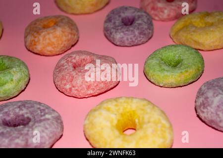 Flache, süße Donuts in verschiedenen Farben, die auf rosa Hintergrund köstlich aussehen Stockfoto