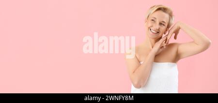 Glückliche, reife Frau in Handtuch auf rosafarbenem Hintergrund mit Platz für Text gewickelt Stockfoto