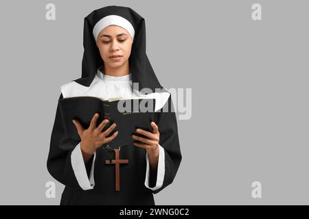 Porträt der jungen Nonne, die Bibel liest, auf grauem Hintergrund Stockfoto
