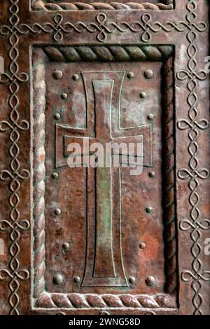 Detail aus einer alten Kirchentür mit Kreuzschilderrelief auf Kupfer Stockfoto