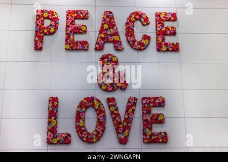 „Frieden und Liebe“ mit leuchtenden roten künstlichen Blumen vor einem Hintergrund weißer Fliesen. Stockfoto