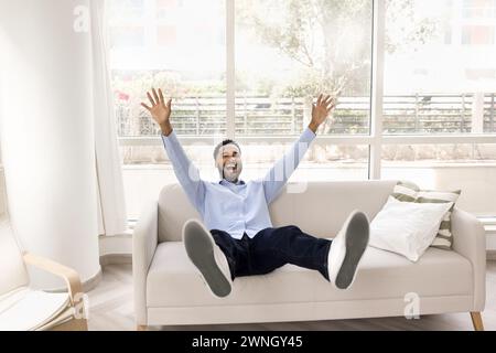 Fröhlicher, glücklicher afrikanischer Mann, der zu Hause auf einer bequemen Couch sitzt Stockfoto