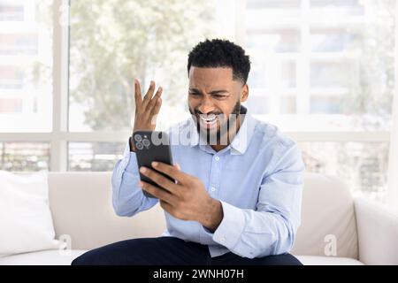Besorgter verzweifelter junger Schwarzer, der Probleme mit dem Handy hat Stockfoto