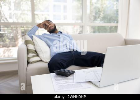 Erschöpfter afroamerikanischer Mann, der zu Hause auf einer weißen Couch schläft Stockfoto