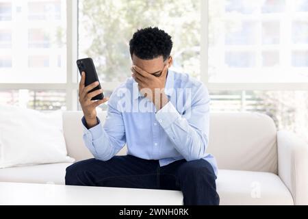 Gestresste Verärgerung schockierte den jungen afroamerikanischen Mann, der ein Smartphone hielt Stockfoto