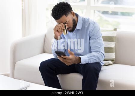 Trauriger afrikanischer Bankkunde mit Handy und Kreditkarte Stockfoto