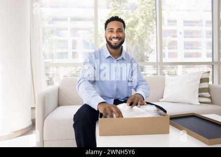 Glücklicher, gutaussehender junger Schwarzer Influencer, der das Paket auspackt Stockfoto