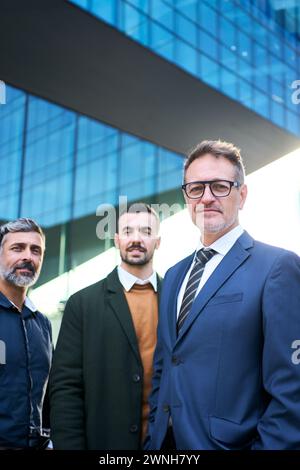 Eine Gruppe Männer in Anzügen, die ein Lächeln teilen, stehen vor einem Gebäude Stockfoto