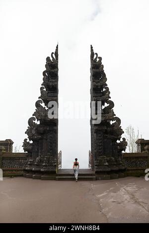 Eine Frau steht am traditionellen balinesischen Tor in den Wolken des heiligen Tempels Pura Pasar Agung Sebudi auf dem Berg Agung Stockfoto