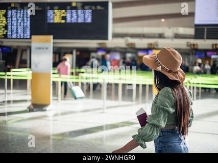 Hispanische Reisender mit Hut, die zum Check-in-Schlange gehen, mit Reisepass in der Hand und Gepäck Stockfoto