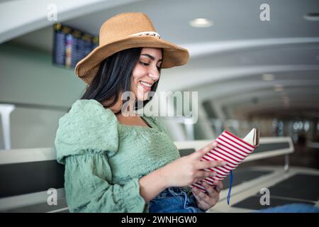 Nahaufnahme einer jungen Latina mit Hut, der ein Buch liest, das im Terminal des Bahnhofs sitzt und wartet Stockfoto