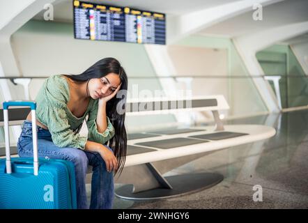 Gelangweilte junge hispanische Frau, die auf den Bänken im Terminal sitzt und ihr Gepäck auf ihren Flug wartet Stockfoto