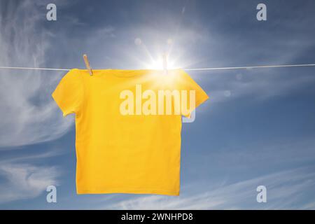 Gelbes T-Shirt, das auf der Wäscheleine vor blauem Himmel trocknet Stockfoto