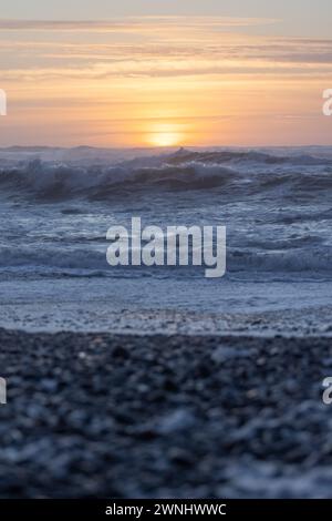 Das Meer ist ruhig und die Sonne untergeht, was eine schöne und ruhige Atmosphäre schafft. Die Wellen sind klein und sanft, und der Himmel ist eine Mischung aus orange A Stockfoto