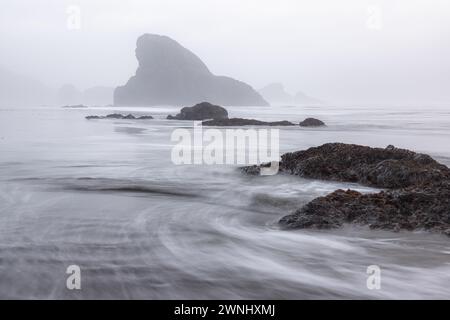 Eine felsige Küste mit einer großen Felsformation im Hintergrund. Das Wasser ist abgehackt und der Himmel ist bedeckt, was eine stimmungsvolle und dramatische Atmosphäre schafft Stockfoto