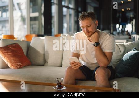 Junger glücklicher Mann, der in der Hotellobby das Handy benutzt. Stockfoto