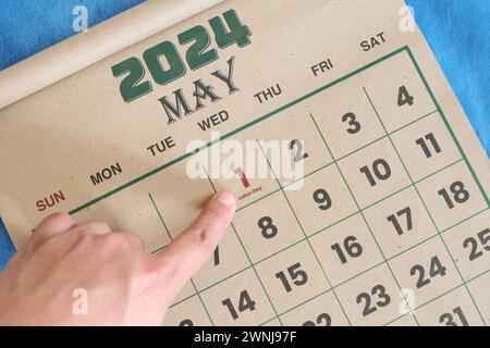 Hand zeigt auf das Datum vom 1. Mai 2024 auf der flachen Kalenderfläche mit blauem Hintergrund. Erinnerung an den Arbeitstag oder den Internationalen Arbeitstag. Stockfoto