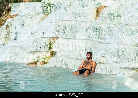 Ein italienischer Mann sitzt in den Wasserkaskaden der heißen Thermalquellen von Saturnia, Toskana, Italien Stockfoto