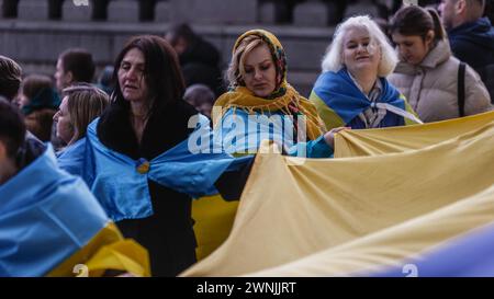 Am zweiten Jahrestag der russischen "Sonderoperation" in der Ukraine halten die Demonstranten eine riesige ukrainische Flagge auf dem Trafalgar-Platz. Stockfoto