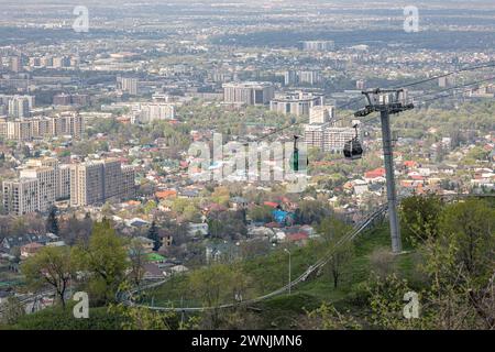 Luftbrücke zum Kok Tobe Hügel in Kasachstan. Seilbahn mit zwei Kabinen, vor dem Hintergrund der Stadt Almaty im Frühling. Touristenort, Stadt Landmar Stockfoto