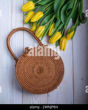 Gelbe Tulpen mit einer gewebten Tasche auf hölzernem Hintergrund. Stockfoto