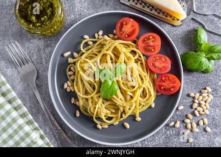 Pasta-Pesto, Spaghetti mit Pesto-Sauce und frischen Basilikumblättern in schwarzer Schüssel auf grauem Betonhintergrund serviert mit Lebensmittelzutaten in Nahaufnahme, Top VI Stockfoto