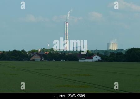 Ein ruhiger Blick auf einen großen Industriekomplex mit Rauchschornsteinen, der sich bei nachlassendem Tageslicht einer ruhigen Landschaft gegenüberstellt. Stockfoto