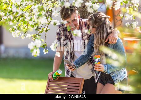 März. 02. 2024 Liptovsky Mikulas. Slowakei - Jugendliche mit Dosen Fanta und Sprite lachen unter dem blühenden Baum im Garten Stockfoto