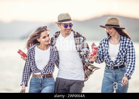 März. 02. 2024 Liptovsky Mikulas. Slowakei - Junge und zwei Mädchen spazieren neben dem Wasser, unterhalten sich und genießen den Tag mit Dosen Coca Co Stockfoto