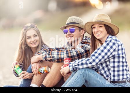 März. 02. 2024 Liptovsky Mikulas. Slowakei – drei junge Menschen genießen im Sitzen und in Ruhe Erfrischungen aus Dosen Coca Cola, Fanta und Sprite Stockfoto