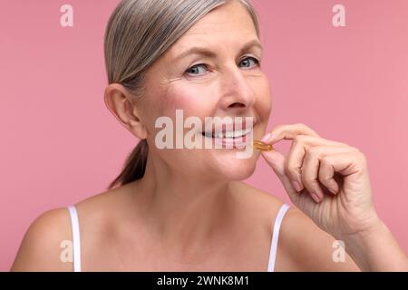 Schöne Frau, die Vitaminkapsel auf rosa Hintergrund nimmt Stockfoto