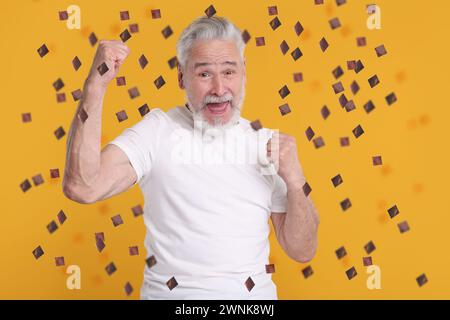 Glücklicher Mann unter fliegendem Konfetti auf orangem Hintergrund Stockfoto