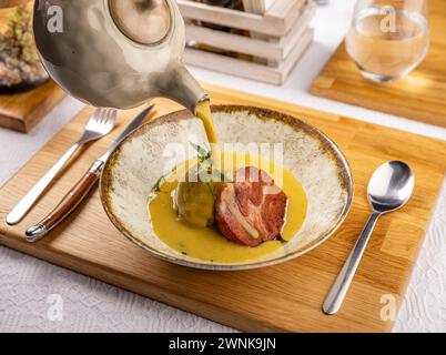 Der Kellner gießt Sahnesuppe in eine gebackene Kartoffel und Räucherschinken Stockfoto