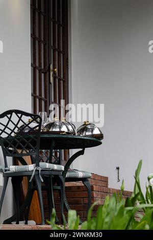 Frühstück auf der Terrasse in der Nähe des Hotelzimmers. Mit Metalldeckeln bedeckte Teller für heißes Geschirr auf dem Tisch. Hotelservice für Besucher. Mahlzeit, RAM-Deckel Stockfoto