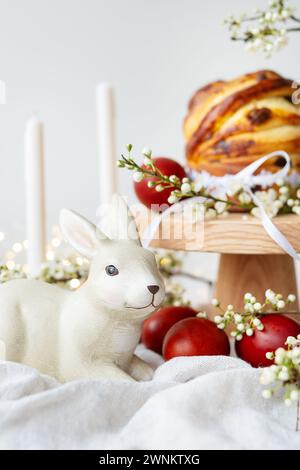 Festlicher Tisch mit Keramikhase, roten Eiern, Kerzen und Ostergebäck. Osterferienkonzept Stockfoto