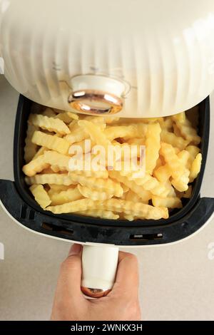 Top View weibliche Hand Pull Air Fritteuse Tablett mit Crinkle Cut Kartoffel Pommes, Kochen ohne Öl, gesunder Lebensstil Stockfoto