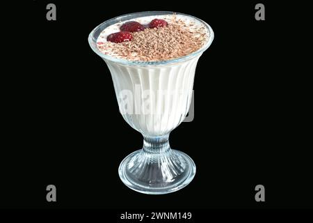 In einem hohen Glas ist Creme mit Schokolade und Himbeeren bestreut, alles auf schwarzem Hintergrund. Stockfoto