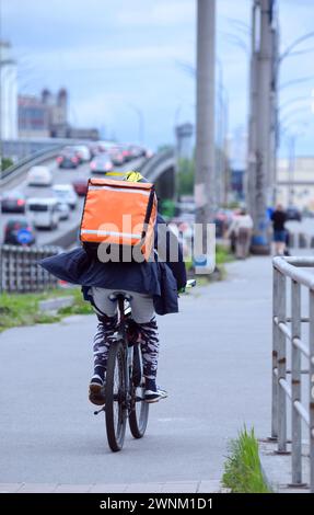 Schneller Expressversand, Kurier fährt schnell Fahrrad auf der Straße der Stadt, Tasche mit Essen auf dem Rücken. Kiew, Ukraine Stockfoto
