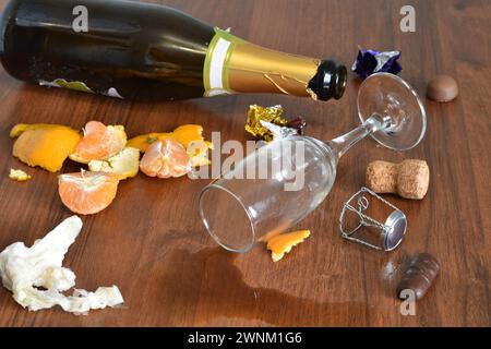 Nach einem lustigen Urlaub blieben eine Flasche, ein Glas mit verschüttetem Wein und eine Schale von Mandarinen auf dem Tisch. Stockfoto