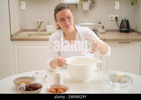Die junge Frau macht Kekse in der Küche zu Hause. Sie trägt Schürze und Brille. Prozess des Kochens von Pekannkuchen in der Küche für American Than Stockfoto